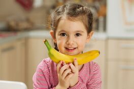 Auf dem Bild ein kleines Mädchen, das sich freut, mit einer Banane in den Händen