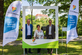 Oberbürgermeister Gerd Härtig, Ortsvorsteherin Annett Groh und Beigeordneter Mario Müller weihen den neuen Bilderrahmen mit Blick auf Schloss Wolkenburg ein